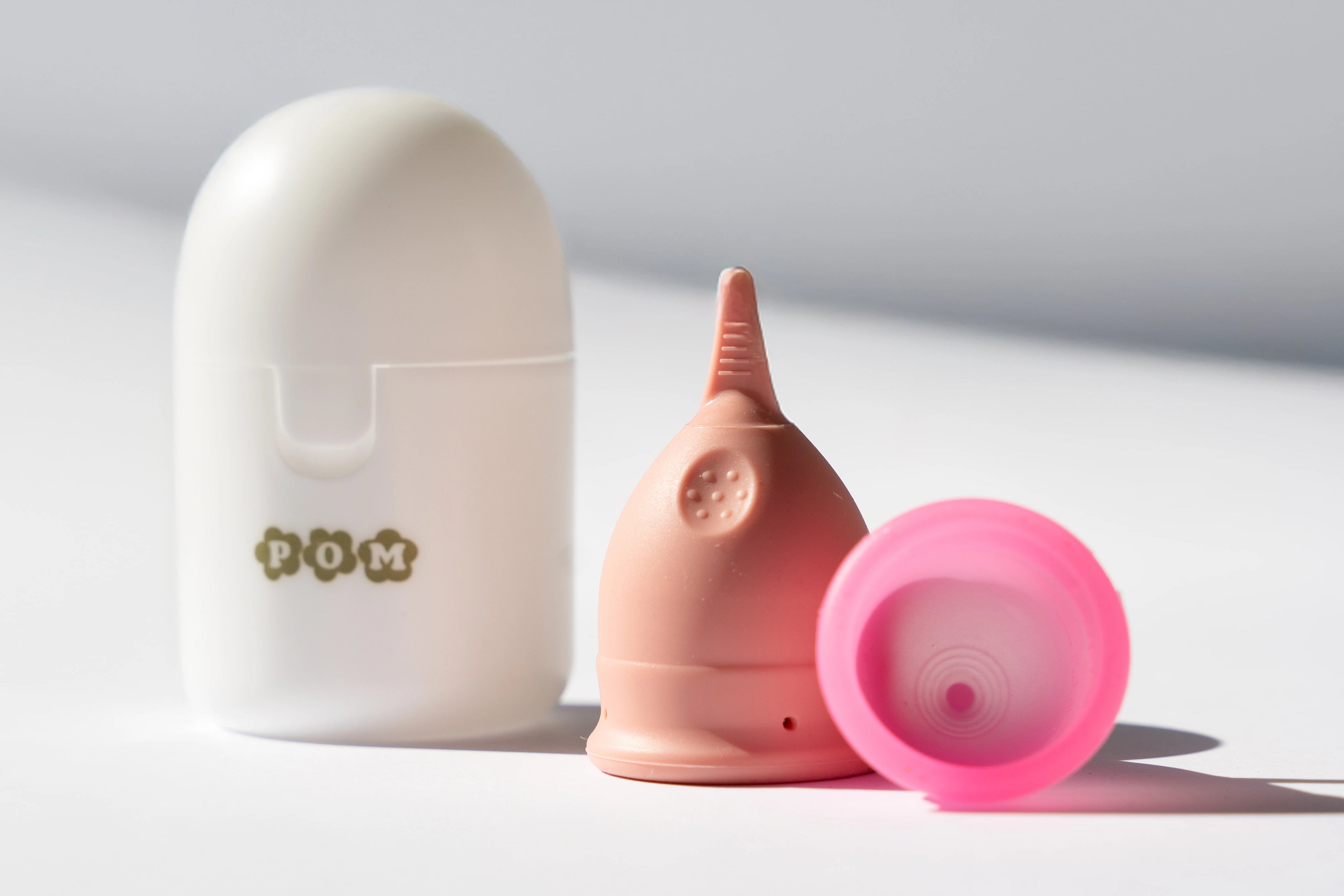 POM period cup steriliser case, POM period cup finger grip style and POM period cup super soft style on a white table
