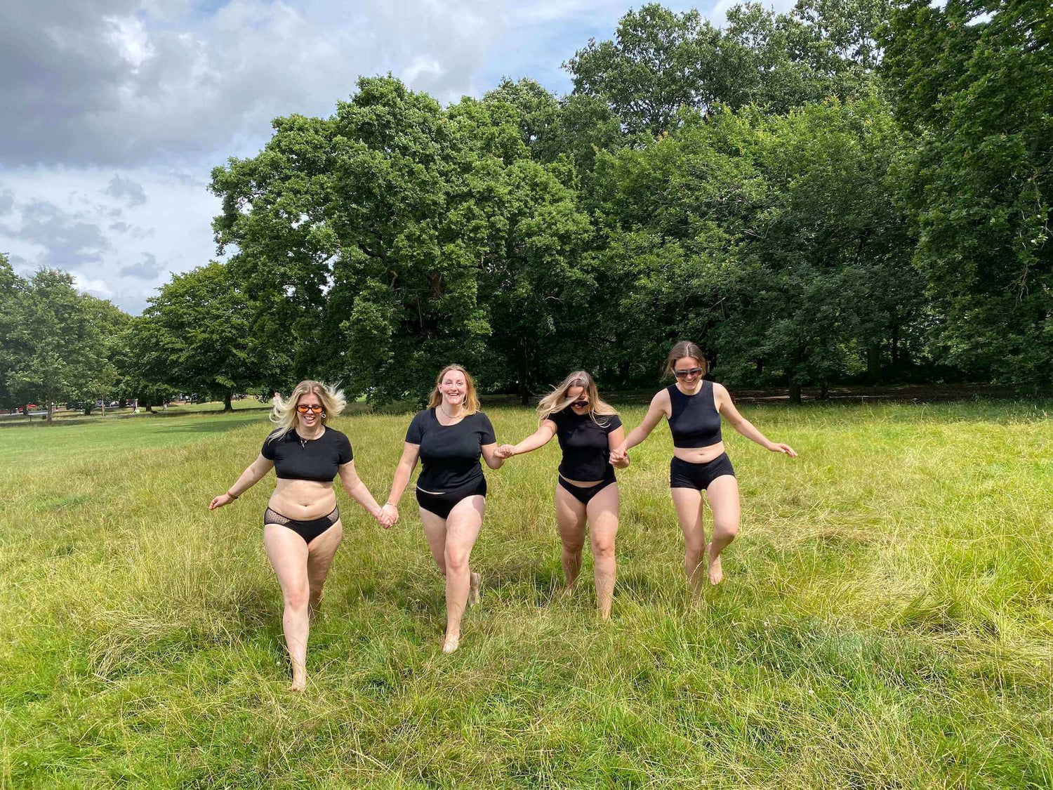 Four women holding hands walking together all wearing black POM period underwear.