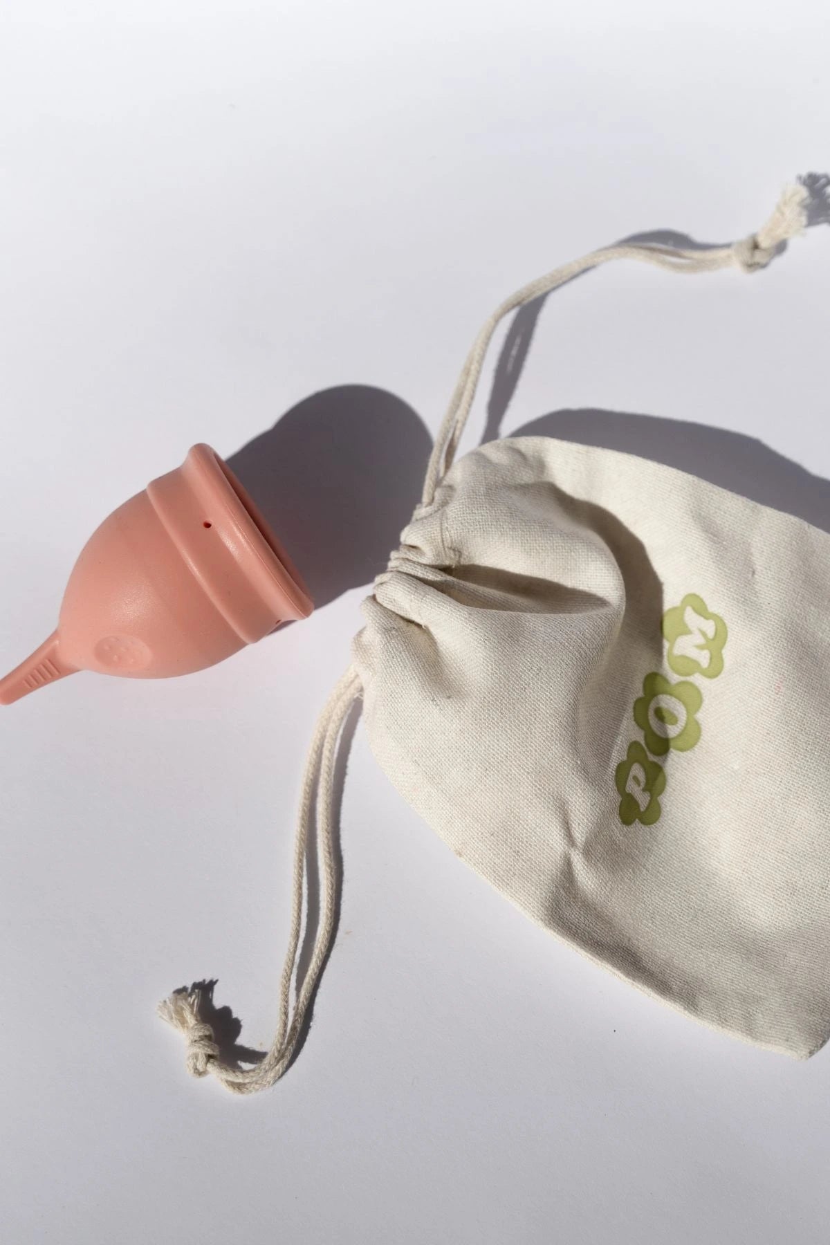 POM Finger Grip Menstrual Cup in light peach, made from 100% medical-grade silicone, shown with its organic cotton travel pouch.