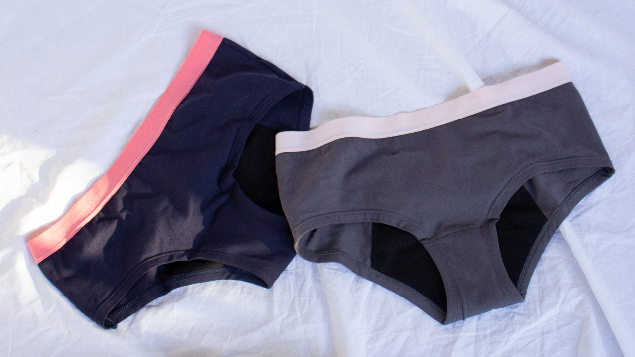 Two pairs of POM teen period underwear lying on a white sheet