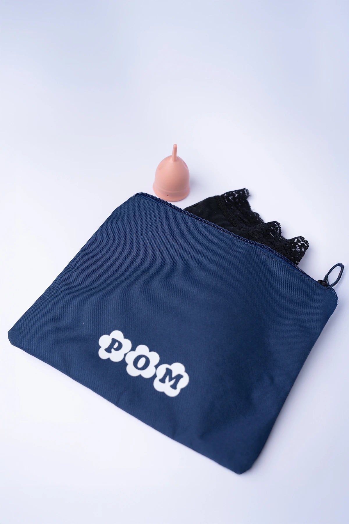 POM Waterproof Toiletry Bag in navy made from rPET (recycled plastic bottles), shown with a pair of POM period underwear and a POM menstrual cup partially visible inside.